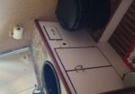 Small bathroom with marble countertop, white cabinets, a black sink, and a toilet with a toilet paper holder nearby.