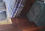 Corner of a small bedroom with a striped blue-gray bed, pillows, and built-in wooden cabinetry; blue carpeted floor nearby.