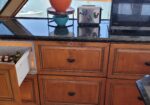 Kitchen counter with wooden cabinets; an open drawer shows bottles and medicines; microwave on the right and a potted bonsai on the left.