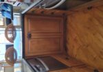 Wooden kitchen cabinets and countertops in a boat or small kitchen, with a built-in dishwasher and oven visible, and water view through the windows behind.