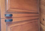 Pair of wooden kitchen cabinet doors with decorative rope trim and black metal handles, under a dark granite countertop.