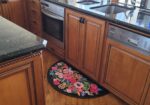 Wooden kitchen cabinetry with black granite counters and built-in stainless oven and dishwasher; a colorful floral rug sits on the floor