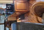 Interior of a yacht galley with wood cabinets, black granite counters, and a microwave on the counter; potted plants and framed photo decorate the space.