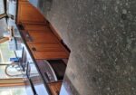 Boat galley with granite countertops, wooden cabinets, and a double sink under large windows overlooking a marina