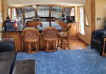 Luxurious boat galley with a dark granite island, four wicker bar stools, and wooden cabinetry; large windows overlook marina.